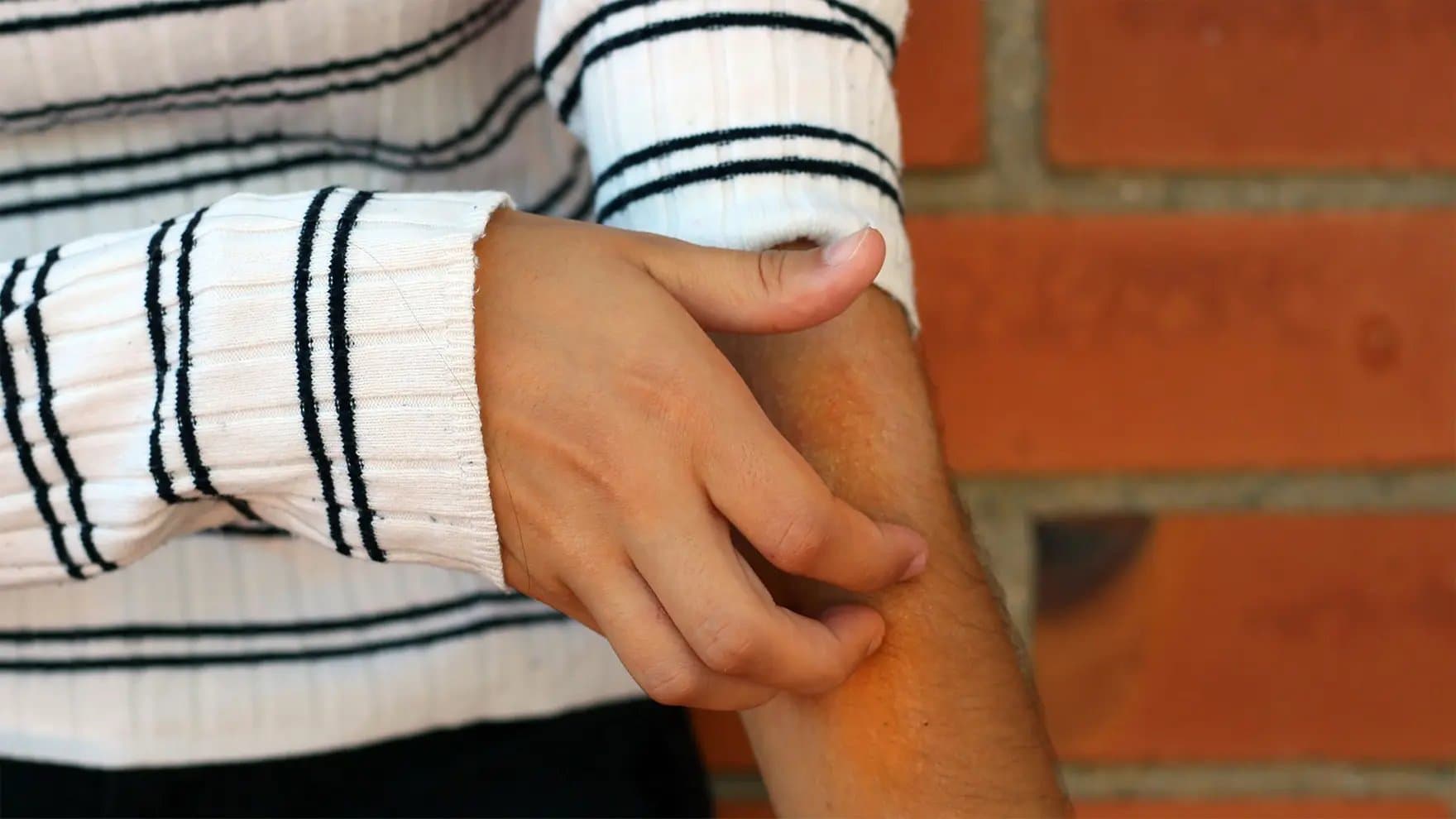 Hands pull up a sleeve on a ribbed, white and black striped sweater. The background is a brick wall.