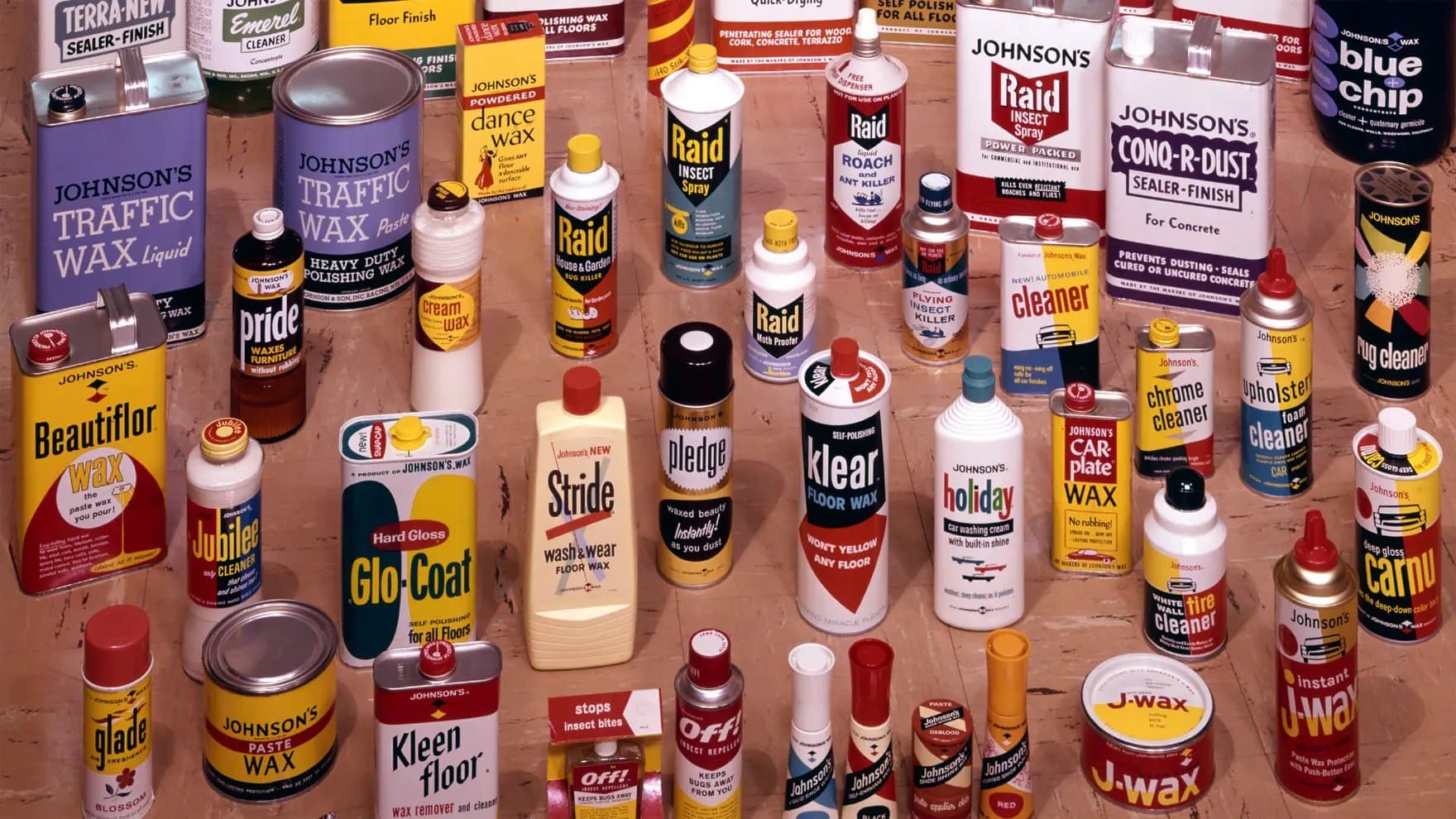 Various cleaning and maintenance products are displayed, including cans and bottles labeled with brands such as Johnson's, Raid, and Pledge. Text includes "TRAFFIC WAX," "INSECT SPRAY," "Glo-Coat," and "J-wax."