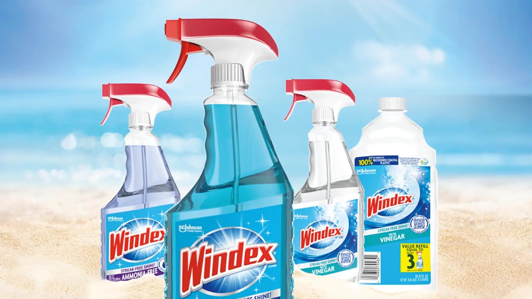 Bottles of Windex spray and refill containers stand on a sandy beach with an ocean backdrop. Text on bottles includes "Windex," "Streak-Free Shine," "Ammonia-Free," "Vinegar," and "Value Refill Equal to 3."
