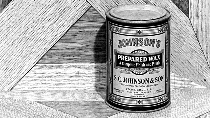 A vintage metal can labeled "Johnson's Prepared Wax" stands on a parquet wood floor. Text: "A Complete Finish and Polish, Manufactured by S.C. Johnson & Son, Racine, Wis., U.S.A."
